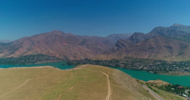 Dağlarla Çevrili Bir Gölün Yanındaki Toprak Yolda Bir Dron Uçuyor — Stok video