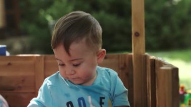 Küçük Avrupalı bir çocuk, yazın sokağın ortasında, tahta bir yiğitte renkli süprüntülerle oynuyor. Yavaş Hareket, Kapat.