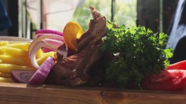 Şef pişmiş et, soğan, otlar, domatesler ve sebzelerle servis edilen ahşap bir tahtayı gösteriyor. Kapat, Yavaş Hareket.