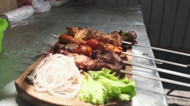 Şef ahşap bir tahtanın üzerinde tavuk, pelerin ve ciğer ile kebap, soğan, bitki, domates ve sebze servis ediyor. Yavaş Hareket, Kapat.