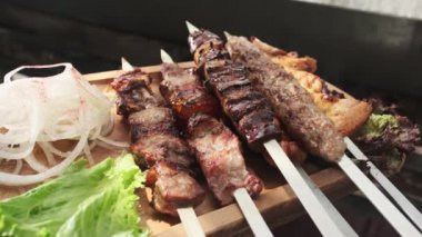 Bir garson ahşap tepsiyi tavuk, et ve ciğer kebabıyla gösteriyor, soğan, bitki ve sebzelerle servis ediliyor. Yavaş Hareket, Kapat.