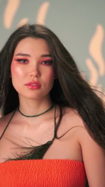 Rüzgarda savrulan uzun saçlı ve parlak makyajlı genç bir kadının dikey portresi. Yavaş Çekim, Kapat, Stüdyo Çekimi.