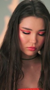 Uzun siyah saçlı ve parlak makyajlı genç bir mankenin dikey portresi. Yavaş Çekim, Kapat, Stüdyo Çekimi.