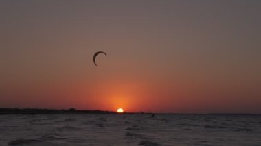 Kiteboarding on the sunset. Man on the kiteboard rides in the evening. Mans silhoulette. Setting sun in the frame.