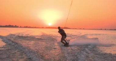 Wakesurfer gölde sörf tahtası kullanıyor. Yakın çekim, deniz mavisi wakeboard, günbatımında çekilmiş..