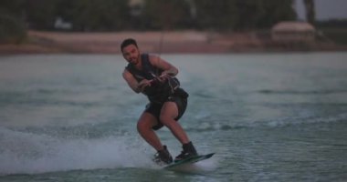 Wakesurfer gölde sörf tahtası kullanıyor. Yakın çekim, deniz mavisi wakeboard, günbatımında çekilmiş..