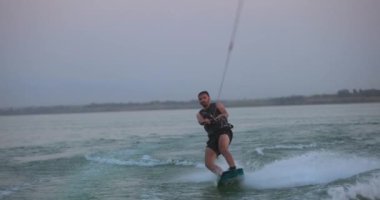 Wakesurfer gölde sörf tahtası kullanıyor. Yakın çekim, deniz mavisi wakeboard, günbatımında çekilmiş..