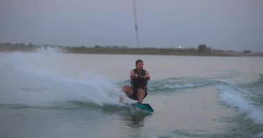 Wakesurfer gölde sörf tahtası kullanıyor. Yakın çekim, deniz mavisi wakeboard, günbatımında çekilmiş..