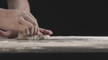 Male hands divide baking dough into three equal shares on a wooden board sprinkled with flour. Filmed on black background