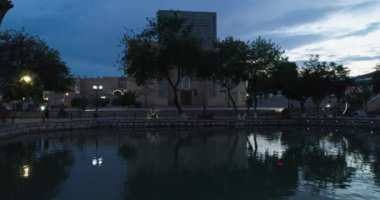 İnsansız hava aracı, geceleri Ulugbek Madrasah antik kompleksi yakınlarında havuz suyunun yüzeyinde uçar. Eski Buhara, Özbekistan. Hava Görünümü.