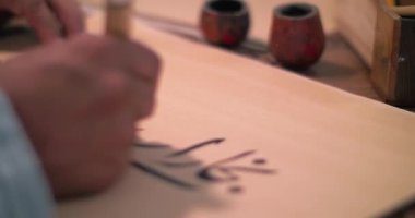Bir kaligraf stilini mürekkebe batırır ve antik teknolojiyi kullanarak parşömen üzerine bir mektup yazar.