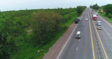 Bir İHA, yol kenarından trafiği başlatan bir kamyonun üzerinden uçuyor. Etrafta ağaçlar ve yeşil alanlar var. Bulutlu bir yaz günü. Hava Görünümü.