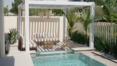 Güneşli bir günde Dubai 'de özel bir villanın arka bahçesinde küçük bir yüzme havuzu ve kanepesi var. Dışarıda ağır çekim.