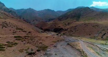 Bir dron dağların ve tepelerin arasında kurumuş bir nehrin üzerinde uçuyor. Hava görüntüsü, yavaş çekim