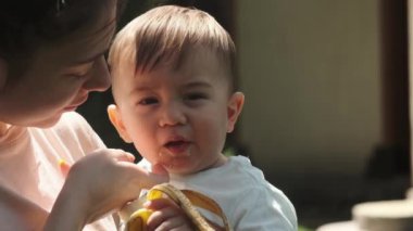 Genç bir annenin kollarında küçük bir çocuk muz yiyor. Yavaş Hareket.