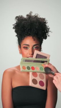 Dubai, BAE - 710 2023: Profesyonel makyaj ustası kıvırcık saçlı genç bir modele boya uyguluyor. Dikey, Yavaş Hareket, Kapat.