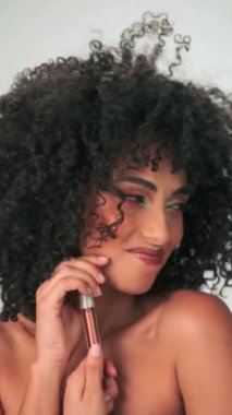 Uzun kıvırcık saçlı ve parlak makyajlı genç bir kadın kirpik boyasını gösteriyor. Dikey, Yavaş Hareket, Yakın çekim, Stüdyo Çekimi.