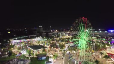 Bir dron lunaparkın üzerinde atlı karınca ve dönme dolap ile uçuyor. Gece, hava manzaralı.