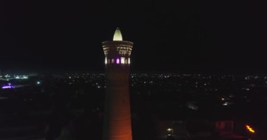 Karmaşık Kalyan Minaresi 'nin aydınlatılmış antik kulesinin yakınında bir dron gece uçar. Buhara, Özbekistan, Havadan görünüm.