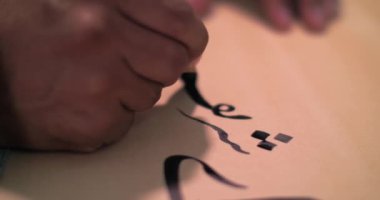 Bir kaligraf stilini mürekkebe batırır ve antik teknolojiyi kullanarak parşömen üzerine bir mektup yazar.