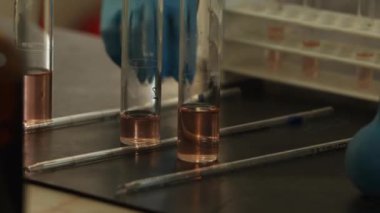 Laboratuvar teknisyeni eldivenler ve koruyucu giysiler içinde laboratuarda pipet ve kimyasal aletlerle çalışıyor. Yavaş Hareket, Kapat.