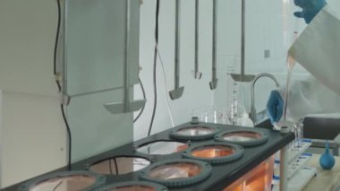Koruyucu giysiler içindeki laboratuvar teknisyeni laboratuardaki otomatik karıştırıcıdan kimyasal örnekler alıyor. Kapat, Yavaş Hareket.