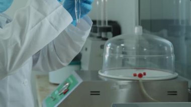 Beyaz önlüklü ve koruyucu eldivenli bir laboratuvar teknisyeni kimyasal bir kaba sıvı döker. Laboratuvar, ağır çekim..