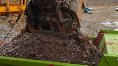 Kömür ocağında büyük bir sanayi kazıcısı bir çöp kamyonuna taş yüklüyor. Kulübeden görüntü. Yavaş Hareket.