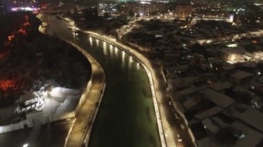 Gece aydınlık bir şehrin ortasındaki nehrin üzerinde bir dron. Hava Görünümü.