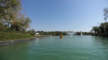 Turistli tekneler kıyıda ağaçlarla birlikte şehir gölünde yelken açıyor. Güneşli bir yaz günü. Yavaş Hareket