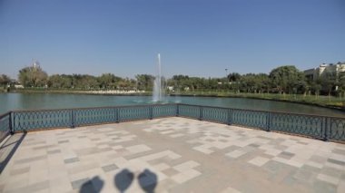 Şehir gölünün üzerinde çeşmelere bakan iskele boyunca bir yürüyüş. Güneşli bir yaz günü. Yavaş Hareket