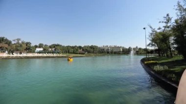 Şehir gölünün üzerinde, çeşmelere bakan ve turistlerle dolu teknelerin önünden geçen bir yürüyüş. Güneşli bir yaz günü. Yavaş Hareket