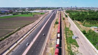Tarlalar ve ağaçlar arasında otoban boyunca giden bir trenin üzerinde bir dron. Güneşli bir yaz günü. Hava Görünümü