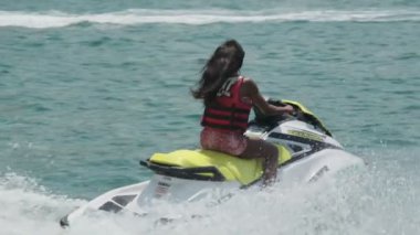 Açık denizlerde jet ski üzerinde can yeleği giymiş esmer bir kadın. Yavaş çekim