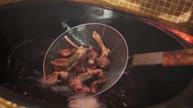 Şef, büyük bir pilav kazanında kaynayan yağın içine slotlu kaşıkla et parçaları koyar. Yavaş Hareket, Kapat.