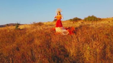 Drone, sonbahar kıyafetiyle günbatımı arka planında dağlardaki çayırlarda genç bir kadının üzerinden uçuyor. Hava görünümü.