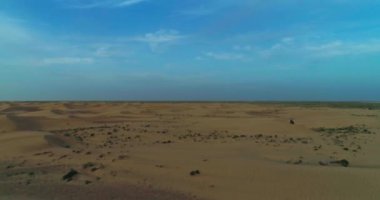 İnsansız hava aracı, Arap kıyafetleri içinde çölün kum tepelerinde gün batımının arka planında yürüyen bir adamın etrafında uçuyor. Hava görünümü.