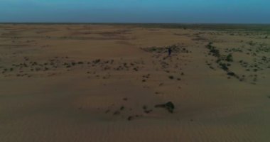 Bir dron Arap kıyafetleri içinde çölün kumullarında gün batımının arka planında yürüyen bir adamın üzerinden uçuyor. Hava Görünümü.