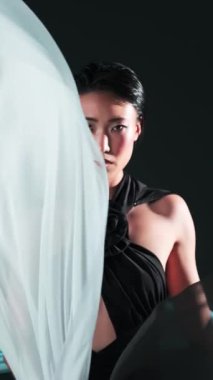 Parlak makyajlı genç Asyalı modelin stüdyo dikey portresi. Etrafında rüzgarda uçuşan ipek parçaları.