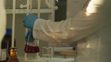 Laboratuvarda cam eşyalar ile çalışan koruyucu giysili laboratuvar teknisyenlerinin elleri. Kapat, Yavaş Hareket.