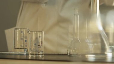 Laboratuvar teknisyeni eldivenler ve koruyucu giysiler içinde laboratuarda pipet ve kimyasal aletlerle çalışıyor. Yavaş Hareket, Kapat.