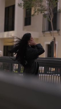 Saçları rüzgarda uçuşan, akşam yürüyüşünde uzun bir yağmurlukla genç bir kadın. Yavaş Hareket