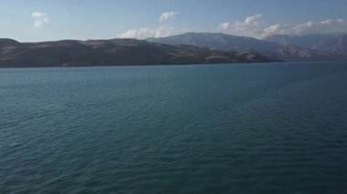 Mavi bir dağ gölünün üzerinde bir dron uçuyor. Güneşli bir yaz günü. Hava Görünümü.