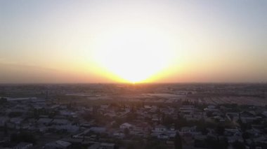 İnsansız hava aracı batan güneşin aydınlattığı evlerin çatılarının üzerinde uçuyor. Şehrin üzerinde bir bahar akşamı. Hava Görünümü.