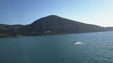 Mavi bir dağ gölünün üzerinde bir dron uçuyor. Turistli bir tekne suda yüzüyor. Güneşli bir yaz günü. Hava Görünümü