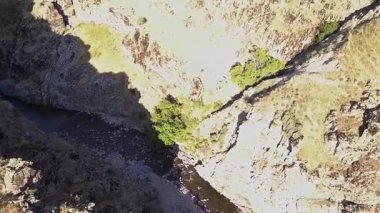 İnsansız hava aracı bir nehirle dağ kanyonunun üzerinden uçuyor. Güneşli bir yaz günü. Hava Görünümü.