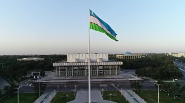 Bir İHA şehrin ortasında dev bir bayrağın üzerinde dalgalanıyor. Gün batımı gökyüzü. Hava Görünümü