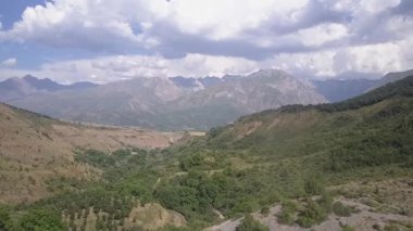 Yeşillik ve çalılarla kaplı dağların tepesindeki bir dron. Bulutlu bir yaz günü. Hava görünümü.