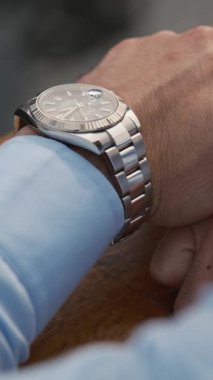 Lüks kol saati olan iş elbiseli genç bir adam pahalı bir premium arabanın yanında duruyor. Dubai 'de bulutlu bir akşam. Kapat, Yavaş Hareket