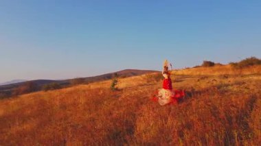 İnsansız hava aracı film ekibi ve sonbahar kıyafetiyle günbatımı arka planındaki dağlarda çayırlarda uçuyor. Hava görünümü.